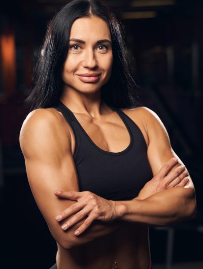 Beautiful female bodybuilder wearing sport clothes and standing with her arms crossed while looking at the camera